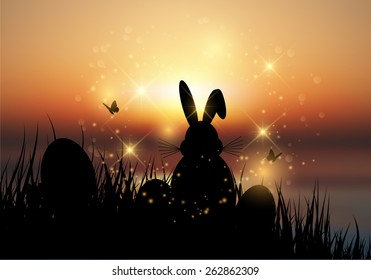 Silhouette of the Easter bunny sat in the grass against a sunset sky