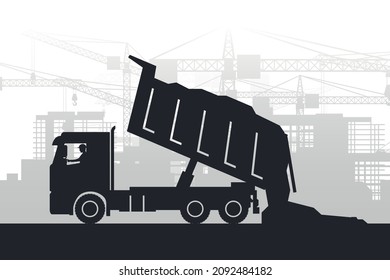 Silhouette of heavy machinery with operator unloading construction materials from truck on background of city with buildings under construction