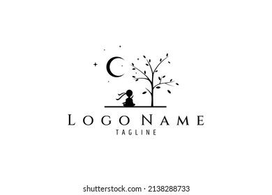 Silhouette logo design of a ninja sitting cross-legged in the shade of a tree on the background of the moon and sparkling stars.