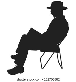 Silhouette of a man reading. He is sitting in a chair and wearing a hat and glasses