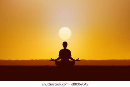 Silhouette of man sitting and meditating on ground under sunset sky background