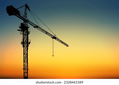 Una grúa de la torre de la silueta para la construcción con un cielo vibrante y luz de la madrugada al fondo.