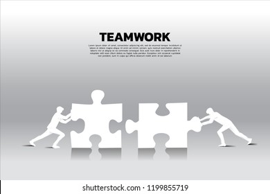 Silhouette of two businessman pushing two jigsaw pieces puzzle. concept of business teamwork.