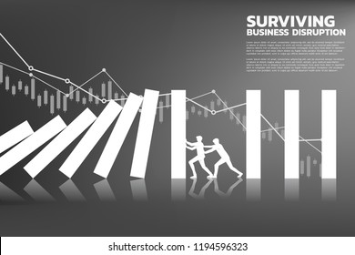 Silhouette of two businessman pushing for stop falling of domino with background graph. business concept of team try to stop the domino effect 