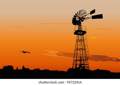 Silhouette of a vintage water pumping windmill against sunset sky