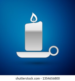 Silver Burning candle in candlestick icon isolated on blue background. Old fashioned lit candle. Cylindrical aromatic candle stick with burning flame. Vector Illustration