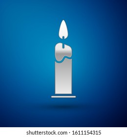 Silver Burning candle in candlestick icon isolated on blue background. Cylindrical candle stick with burning flame.  Vector Illustration