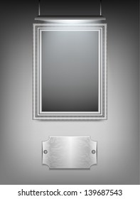 Silver frame hanging on the wall. The lamp that illuminates the painting and the metal plate.