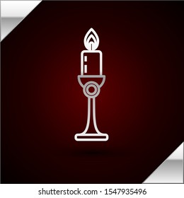 Silver line Burning candle in candlestick icon isolated on dark red background. Old fashioned lit candle. Cylindrical candle stick with burning flame.  Vector Illustration