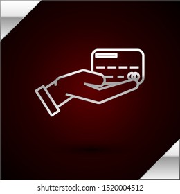 Silver line Human hand holding with credit card icon isolated on dark red background. Online payment. Pay by card. Financial operations.  Vector Illustration