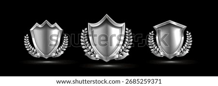 Silver shield emblem set with ribbon and laurel wreath for premium awards or certificates. Metallic heraldic badges with decorative leaves on black. Trophy elements for achievement and victory design.