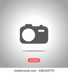 Simple photo camera. Technology icon. Icon under spotlight. Gray background