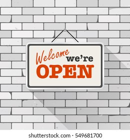 Simple white sign with text 'Come in we're open' hanging on a gray brick wall. Grunge brickwork background, textured rough surface. Creative business interior template for shop, store, supermarket.