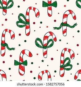 Simplistic Christmas seamless half drop repeat pattern with hand drawn sketched doodled candy canes with green bow ties on a cream background surrounded by red green round and star confetti