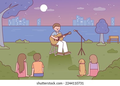 Un cantante tocando una guitarra acústica está en el parque. La gente está sentada en el césped escuchando música.