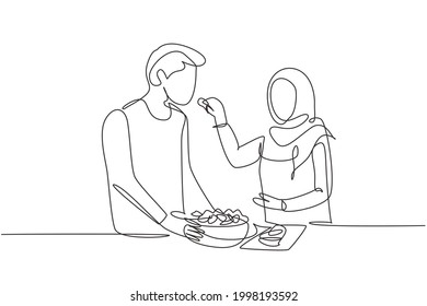 Single continuous line drawing beautiful Arab wife feeds her husband food   in front him is bowl filled and salad  Cooking together in kitchen  One line draw graphic design vector illustration