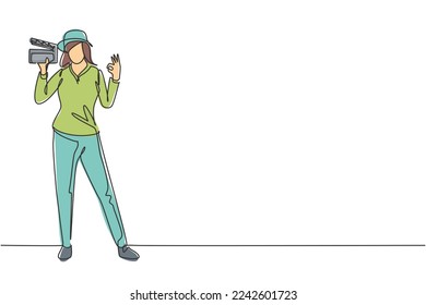 Single continuous line drawing female film director stands with gesture okay holding clapperboard and prepare camera crew for shooting at studio. One line draw graphic design vector illustration