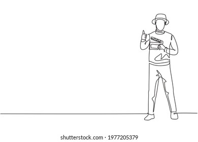 Single continuous line drawing film director stands with a thumbs-up gesture while holding the clapperboard to prepare the camera crew for shooting. One line draw graphic design vector illustration.