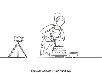 Single continuous line drawing girl baking and decorating cake at kitchen. Woman blogger recording video on camera, using tripod, posting it on social media. One line draw design vector illustration