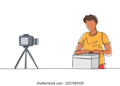 Single continuous line drawing male vlogger unbox and review product live on youtube in studio. Social media influencer recording unboxing video at home. One line draw design vector illustration