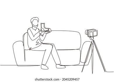Una línea contínua dibujando influencias en medios sociales revisando botas. Joven árabe sonriente vloqueando sobre zapatos deportivos masculinos y grabándose en casa con una cámara de video. vector de diseño de trazos de una línea