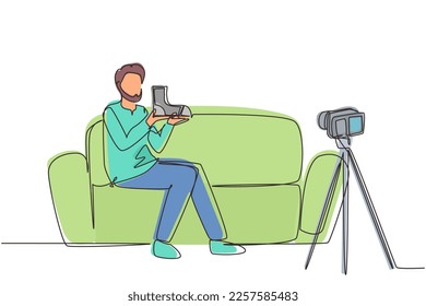 Single continuous line drawing social media influencer reviewing boots. Smiling young Arab man vlogging about men's sports shoe and filming himself at home on video camera. One line draw design vector