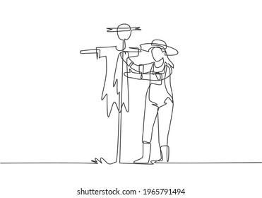 Single continuous line drawing a young female farmer in a straw hat putting up scarecrow to keep out pests of birds. Farming minimalist concept. One line draw graphic design vector illustration.