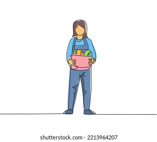 Single continuous line drawing young female farmer standing on farm field and bring basket with full of fruits. Farming minimalism concept. Dynamic one line draw graphic design vector illustration.