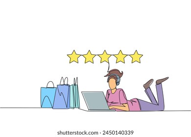 Single continuous line drawing young smiling woman on stomach while typing on laptop. Next to the laptop is a shopping bag. Give the best review with pleasure. One line design vector illustration