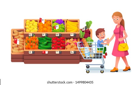 Single mother push full shopping cart with son kid sitting in trolley walking in supermarket fruit & vegetables groceries produce aisle. Mom & child family in grocery store flat vector illustration