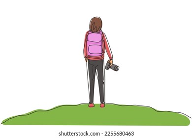 Single one line drawing back view woman holding camera standing on hill of mountain in forest landscape view with sunset. Young tourist photographer. Continuous line draw design vector illustration