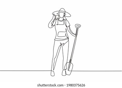 Single one line drawing of female farmer stood with a thumbs-up gesture, wearing a straw hat and carrying a shovel to plant crops on farmland. Continuous line draw design graphic vector illustration.
