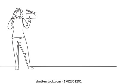 Single one line drawing female film director stands with call me gesture holding clapperboard and prepare camera crew for shooting at studio. Continuous line draw design graphic vector illustration