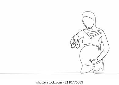 Single one line drawing small shoes for unborn baby in belly of pregnant woman. Arabian pregnant woman holding small baby shoes relaxing at home in bedroom. Continuous line draw design graphic vector