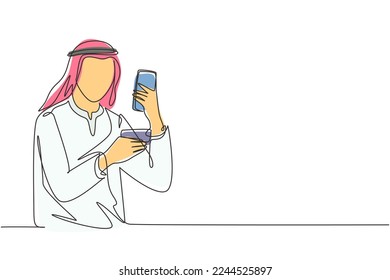 Single one line drawing young Arab man typing entering credit card code on smartphone around desk. Digital lifestyle and payment concept. Modern continuous line draw design graphic vector illustration