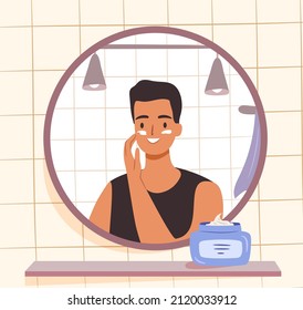 Skincare routine concept. Man applying face cream in bathroom. Happy young guy looking at mirror