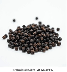 A small pile of dark brown peppercorns sits in the center of a white background, with a few peppercorns scattered around the main pile.