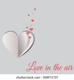 Small red hearts coming out of a folded paper heart shape on gray background for Happy Valentine's Day celebrations. Love in the air text message