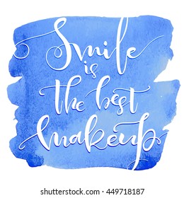 Smile is the best makeup. Inspirational quote handwritten with black ink and brush on blue watercolor stain, custom lettering for posters, t-shirts and cards. Vector calligraphy isolated on white 