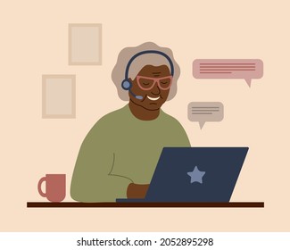 A smiling African grandmother in headphones with a laptop. An elderly woman communicates, studies, works or shoppes online.
