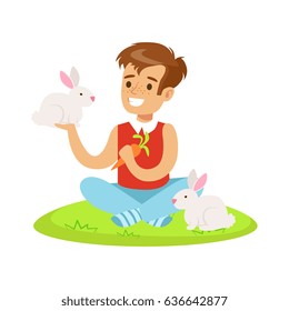 Smiling boy sitting on green grass, playing and feeding two white rabbits with carrot. Colorful cartoon character vector Illustration