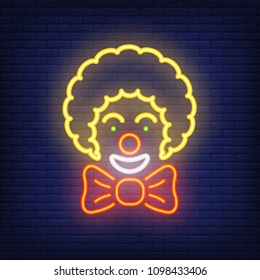 Smiling clown neon icon. Circus artist with big bow on dark brick wall background. Night bright advertisement. Vector illustration in neon style for entertainment or performance poster