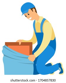 Smiling delivery worker man wearing blue uniform unpacking box isolated on white. Moving house, carton container, furniture banner vector illustration