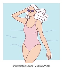 A smiling elderly white woman with long white hair wears sunglasses and a pink swimsuit while walking along the beach.
