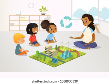 Smiling female kindergarten teacher and children sit on floor and explore toy model with renewable or sustainable energy systems, wind and solar eco friendly power stations. Vector illustration.