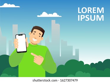 smiling guy with a phone on the background of the city, skyscrapers; shows a blank screen of the phone, points to it with a finger; copy space horizontal
