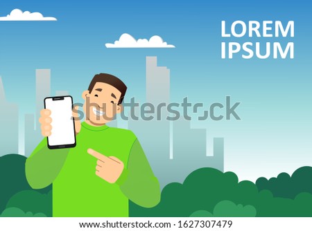 smiling guy with a phone on the background of the city, skyscrapers; shows a blank screen of the phone, points to it with a finger; copy space horizontal