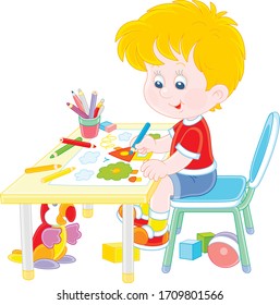 Smiling little boy sitting at his table and drawing with color pencils a funny picture of a small village house and an apple tree on a sunny summer day, vector cartoon illustration