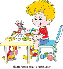 Smiling little boy sitting at his table and drawing with color pencils a funny picture of a small village house and an apple tree on a sunny summer day, vector cartoon illustration