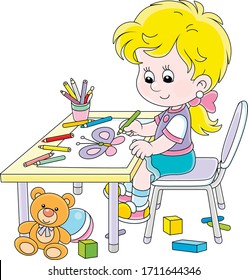 Smiling little girl sitting at her table among toys and drawing with color pencils a funny picture of a small beautiful butterfly, vector cartoon illustration on a white background